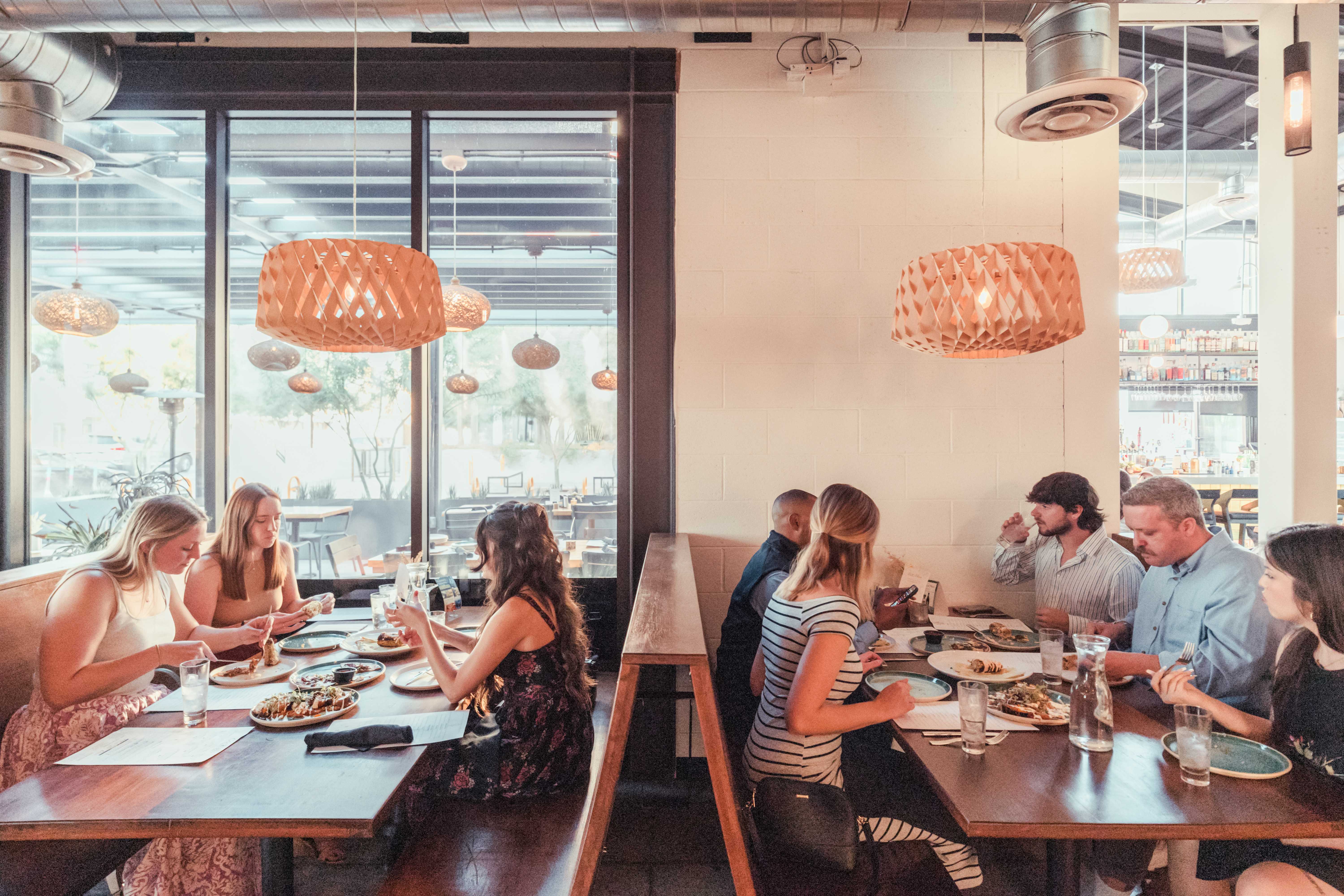 Group of people seated in a modern restaurant booth, sharing food under hanging woven pendant lights