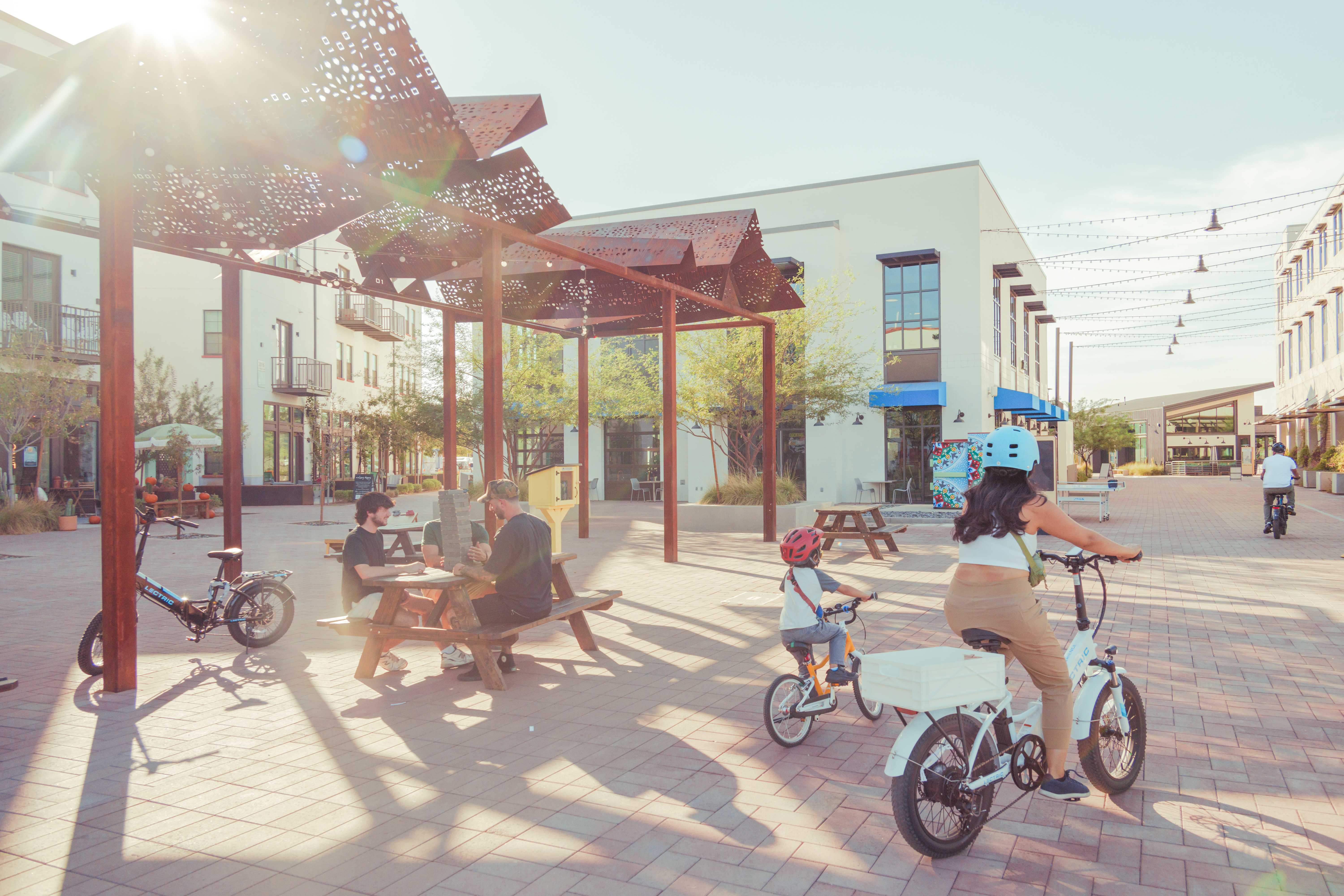 Families and neighbors biking in a sunlit Culdesac Tempe courtyard with decorative shade canopies